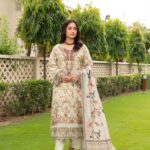 Model wearing Munira Designers Lubna Dhanak Vol 15 cream floral printed and embroided dhanak suit with printed wool shawl, front view